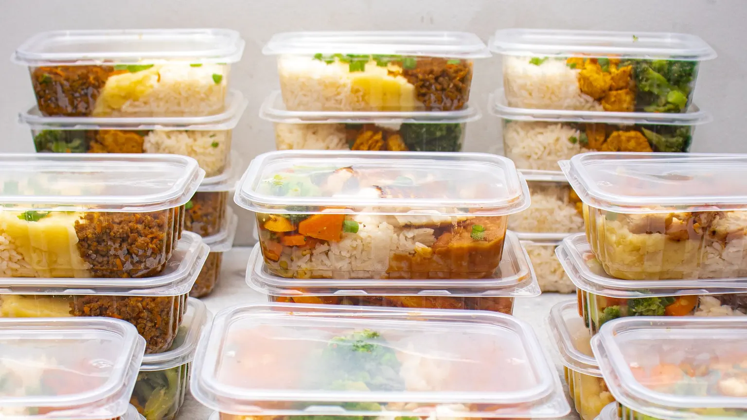 Nhiều hộp suất ăn giống nhau xếp thành hàng, mỗi hộp có cơm, món mặn và rau